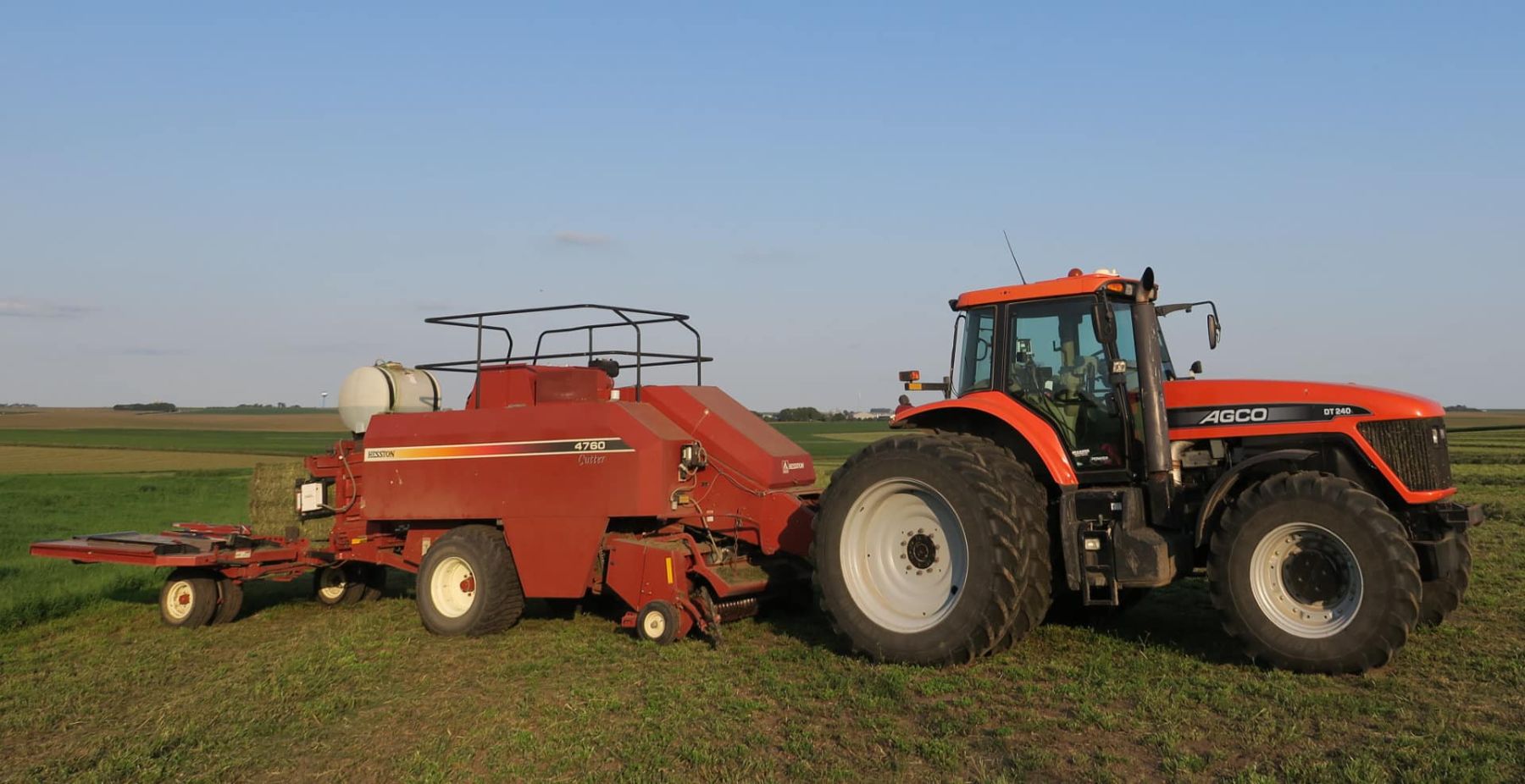 AGCO tractor pulling a round baler through a hay field at dusk
